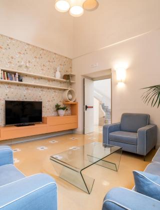 Modern living room with blue sofas, glass table, and plants.